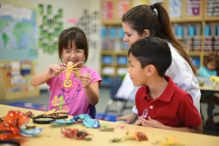Preschool children in a classroom working with educational science materials while teacher assists, showing hands-on learning activities